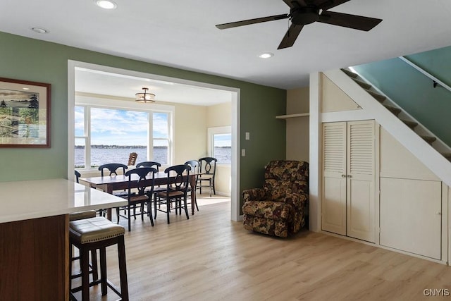 dining area with light wood-style floors, recessed lighting, a water view, and stairway