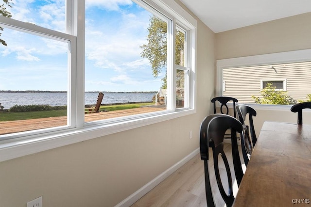 dining area with a water view, light wood-style floors, and baseboards