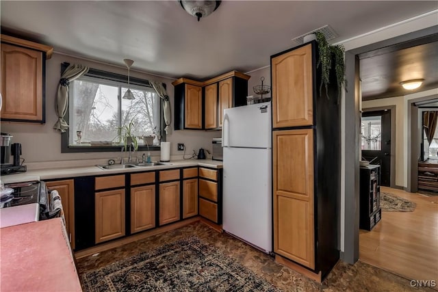 kitchen with a sink, visible vents, light countertops, freestanding refrigerator, and brown cabinets