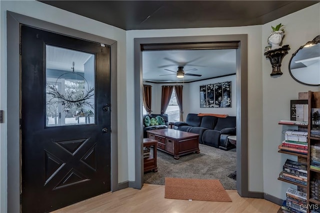 foyer entrance with light wood-style floors, ceiling fan, and baseboards