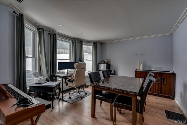 dining room featuring light wood finished floors, baseboards, visible vents, and crown molding