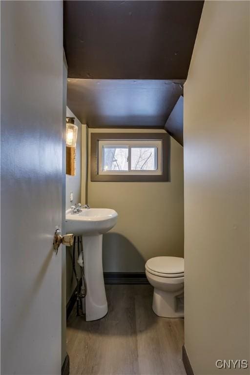 bathroom with baseboards, vaulted ceiling, toilet, and wood finished floors