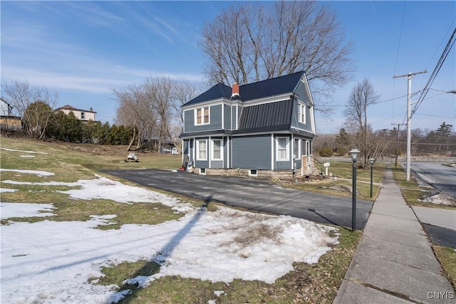 view of front of house with driveway, a chimney, and a gambrel roof