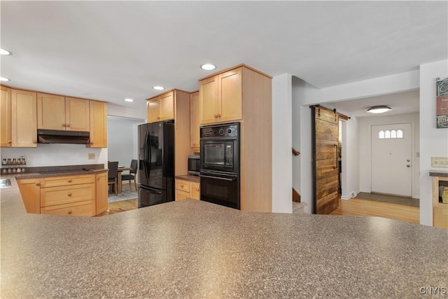 kitchen featuring light brown cabinetry, under cabinet range hood, black appliances, and a barn door