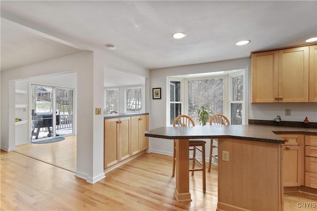 kitchen featuring dark countertops, light wood-style floors, light brown cabinets, and a kitchen breakfast bar