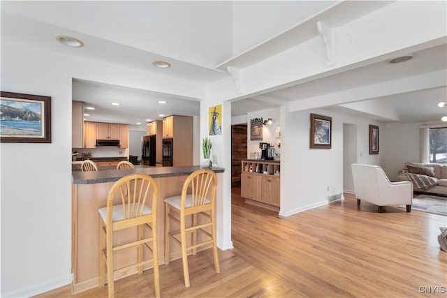 kitchen featuring under cabinet range hood, light wood-style floors, open floor plan, fridge, and dark countertops