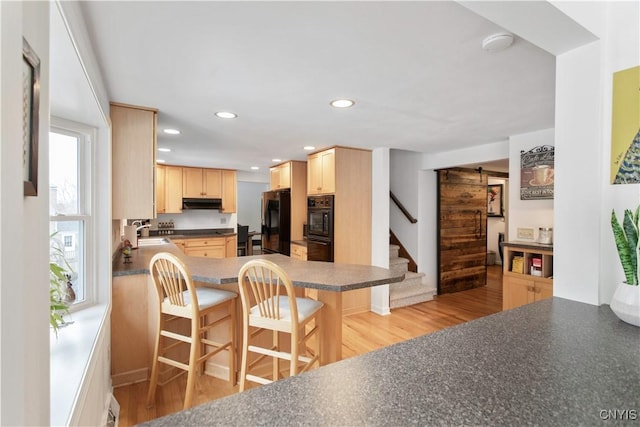 kitchen with recessed lighting, light brown cabinetry, black appliances, light wood finished floors, and dark countertops