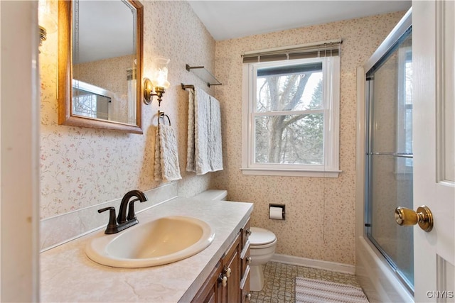 bathroom featuring shower / bath combination with glass door, toilet, vanity, baseboards, and wallpapered walls