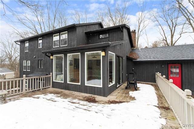 snow covered property featuring a sunroom, fence, a chimney, and a wooden deck