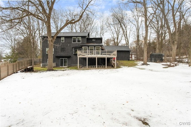 snow covered rear of property with fence and a deck