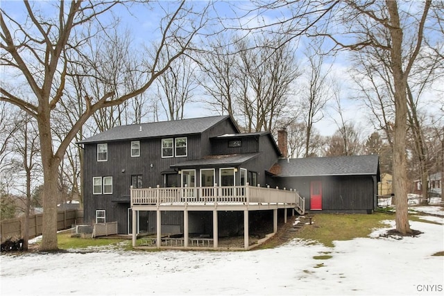 snow covered house featuring a deck, a chimney, and fence