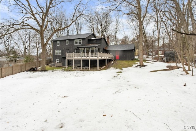 snow covered back of property featuring a chimney, fence, and a deck