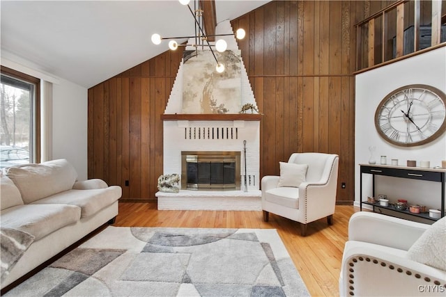 living room with a notable chandelier, a fireplace, wooden walls, wood finished floors, and high vaulted ceiling