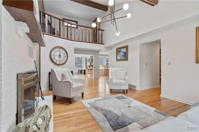 living area with a fireplace, wood finished floors, visible vents, beam ceiling, and an inviting chandelier