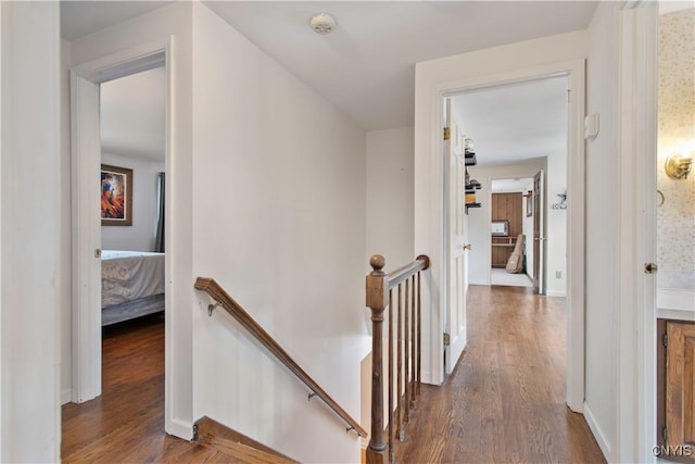 hall featuring dark wood-style floors, baseboards, and an upstairs landing