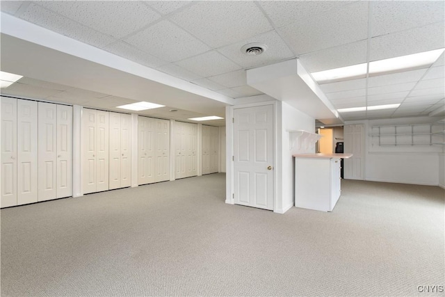 finished below grade area with a drop ceiling, visible vents, and light colored carpet