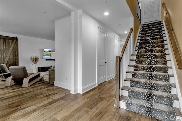 stairs featuring a barn door, baseboards, wood finished floors, and recessed lighting