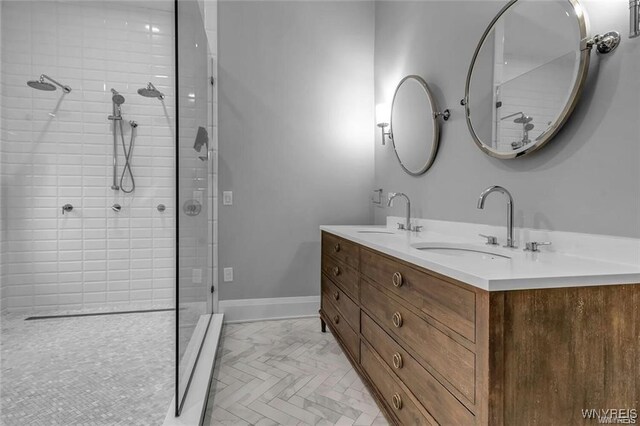 bathroom with double vanity, baseboards, a sink, and tiled shower