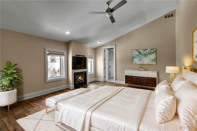 bedroom featuring lofted ceiling, visible vents, a glass covered fireplace, wood finished floors, and baseboards