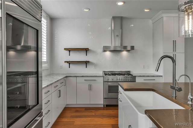 kitchen featuring gas range, dark wood-style flooring, wall chimney range hood, a sink, and recessed lighting