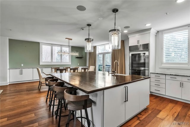 kitchen featuring built in refrigerator, dark countertops, dark wood-style flooring, and a sink