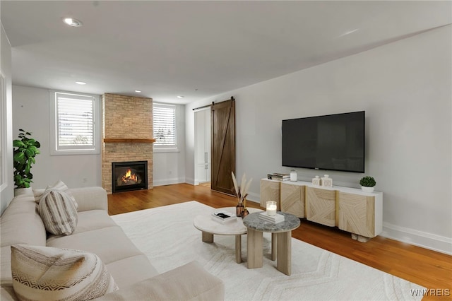 living room with a large fireplace, a barn door, baseboards, wood finished floors, and recessed lighting