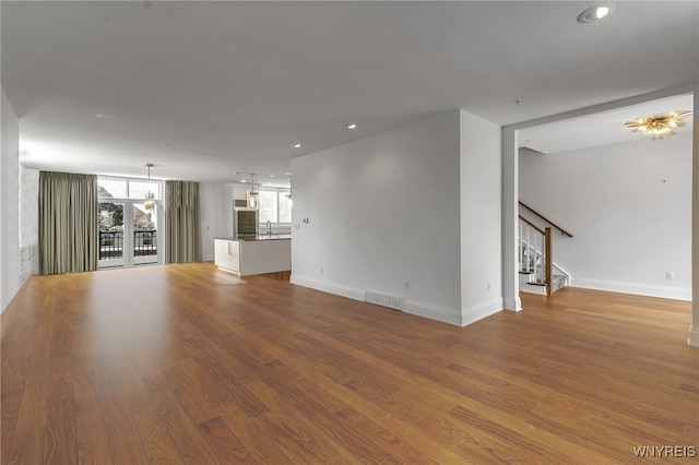 unfurnished living room featuring baseboards, visible vents, stairway, wood finished floors, and a sink