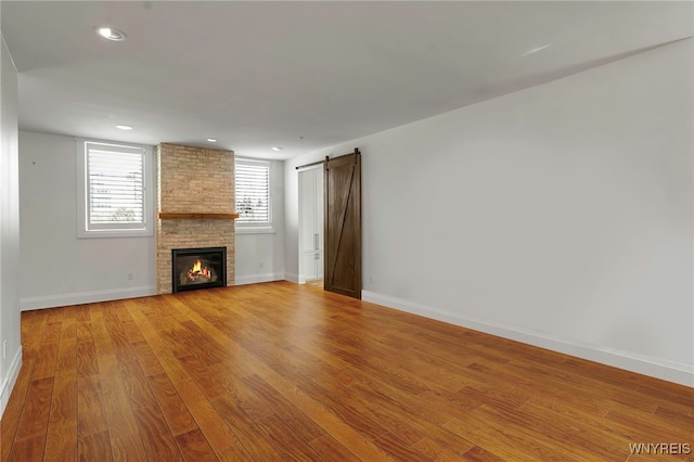 unfurnished living room featuring a fireplace, recessed lighting, a barn door, light wood-type flooring, and baseboards