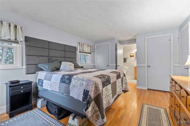 bedroom with light wood finished floors, multiple windows, and ensuite bath