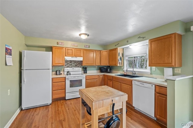 kitchen with white appliances, under cabinet range hood, light wood finished floors, and a sink