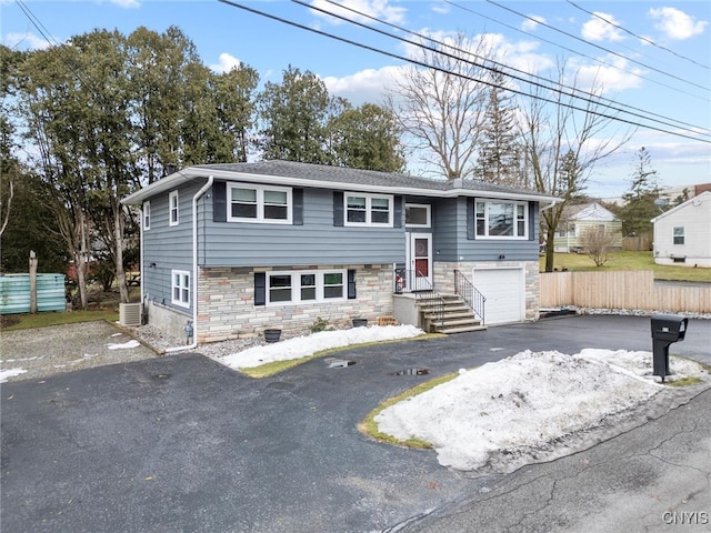 split foyer home with an attached garage, cooling unit, fence, driveway, and stone siding