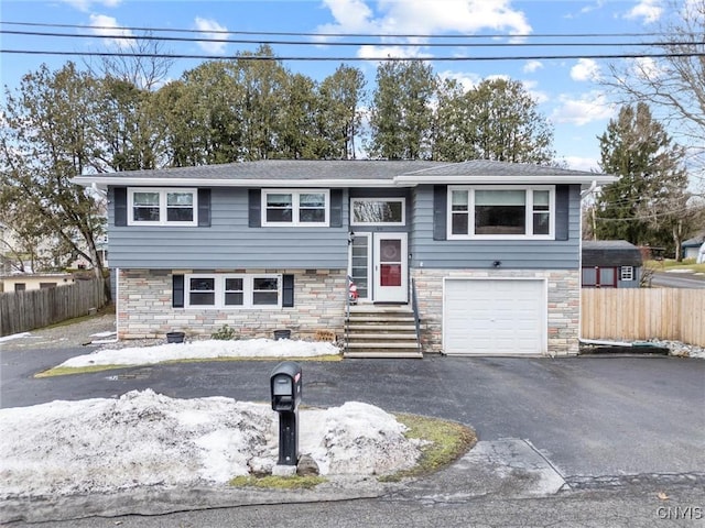 split foyer home with aphalt driveway, stone siding, fence, and an attached garage