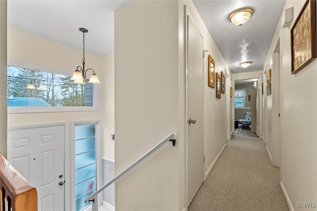 hall featuring baseboards, a notable chandelier, and light colored carpet