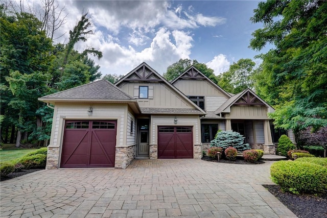 craftsman house featuring a garage, stone siding, decorative driveway, roof with shingles, and board and batten siding