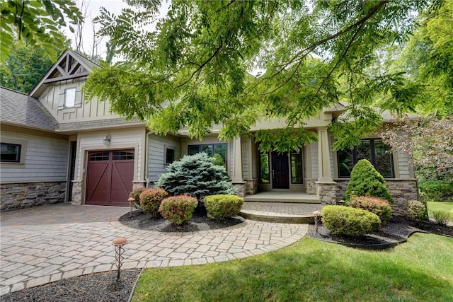 view of front of home with a shingled roof, stone siding, driveway, and an attached garage