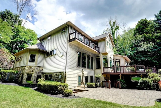 back of house featuring a patio, a yard, stone siding, and a balcony