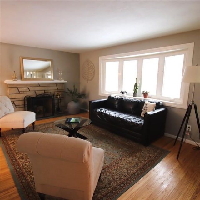 living room featuring a stone fireplace, wood finished floors, and baseboards