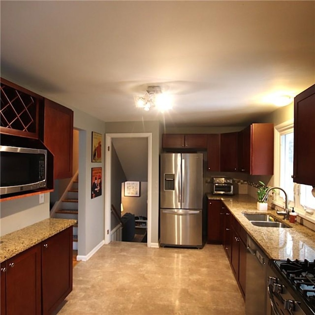 kitchen featuring baseboards, light stone counters, stainless steel appliances, and a sink