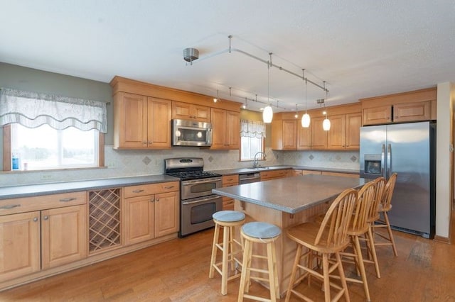 kitchen featuring a kitchen bar, stainless steel appliances, light wood-type flooring, and a wealth of natural light