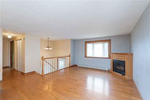 unfurnished living room featuring light wood-type flooring, a baseboard heating unit, a notable chandelier, and a glass covered fireplace