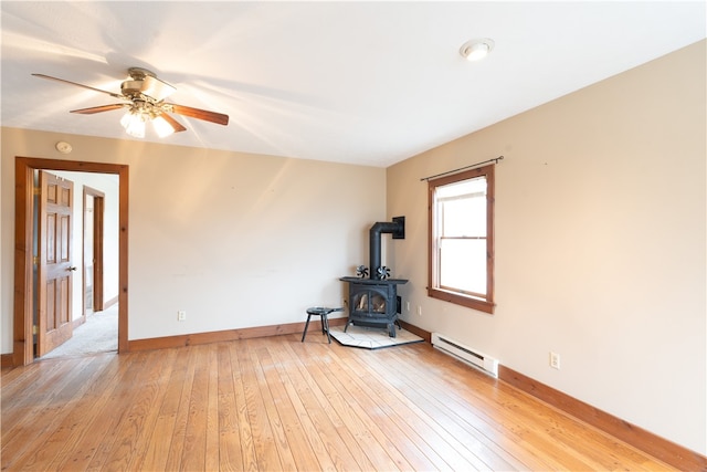 spare room featuring light wood finished floors, a baseboard heating unit, baseboards, a wood stove, and a ceiling fan