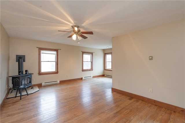 empty room with a wood stove, light wood-type flooring, and a baseboard radiator