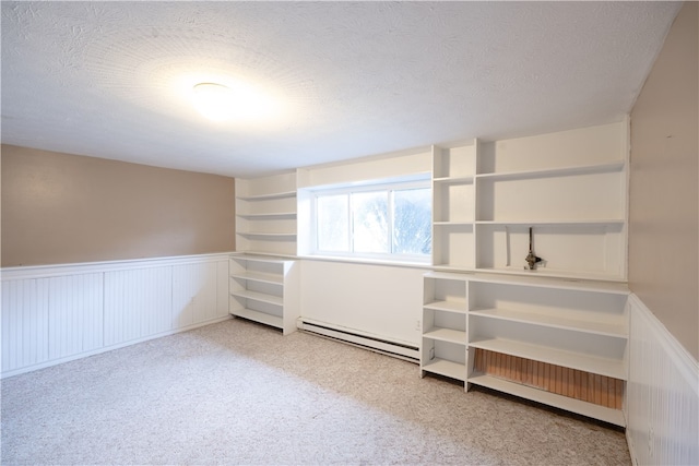 spare room with a textured ceiling, light carpet, wainscoting, and a baseboard radiator