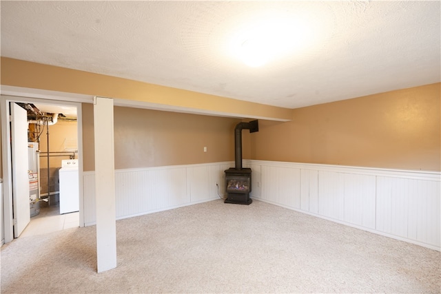 finished basement featuring washer / clothes dryer, water heater, carpet floors, wainscoting, and a wood stove