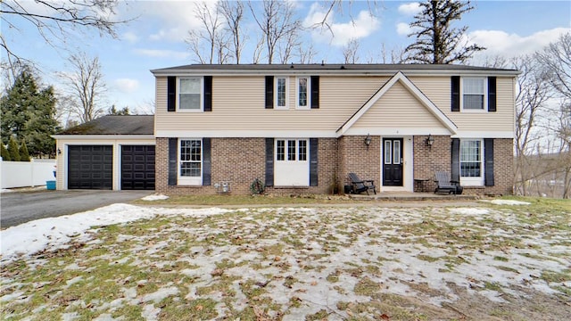 colonial inspired home with aphalt driveway, brick siding, fence, and an attached garage