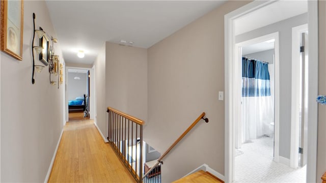 corridor with light wood finished floors, an upstairs landing, and baseboards