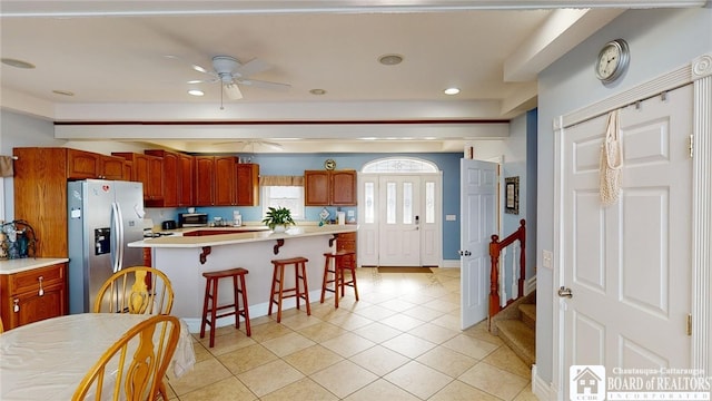 kitchen with a breakfast bar area, light countertops, appliances with stainless steel finishes, a ceiling fan, and light tile patterned flooring