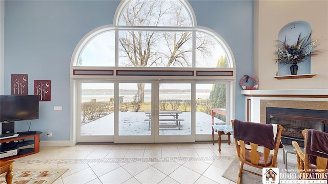 entryway with a towering ceiling, baseboards, a glass covered fireplace, and tile patterned floors