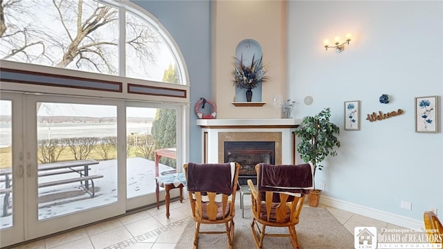 sitting room featuring a high ceiling, tile patterned flooring, a glass covered fireplace, and baseboards