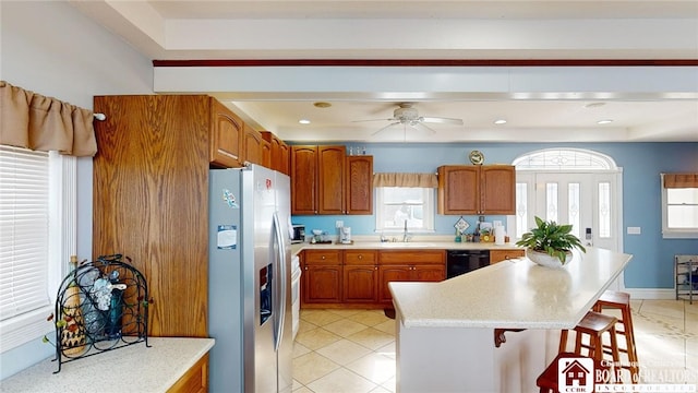 kitchen with black dishwasher, stainless steel fridge, a breakfast bar, light countertops, and a sink